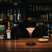 バーカウンターに置かれたピンク色のコスモポリタンカクテルの写真