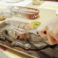 熱々の鉄板でジューと音を立てるステーキの焼ける光景の写真