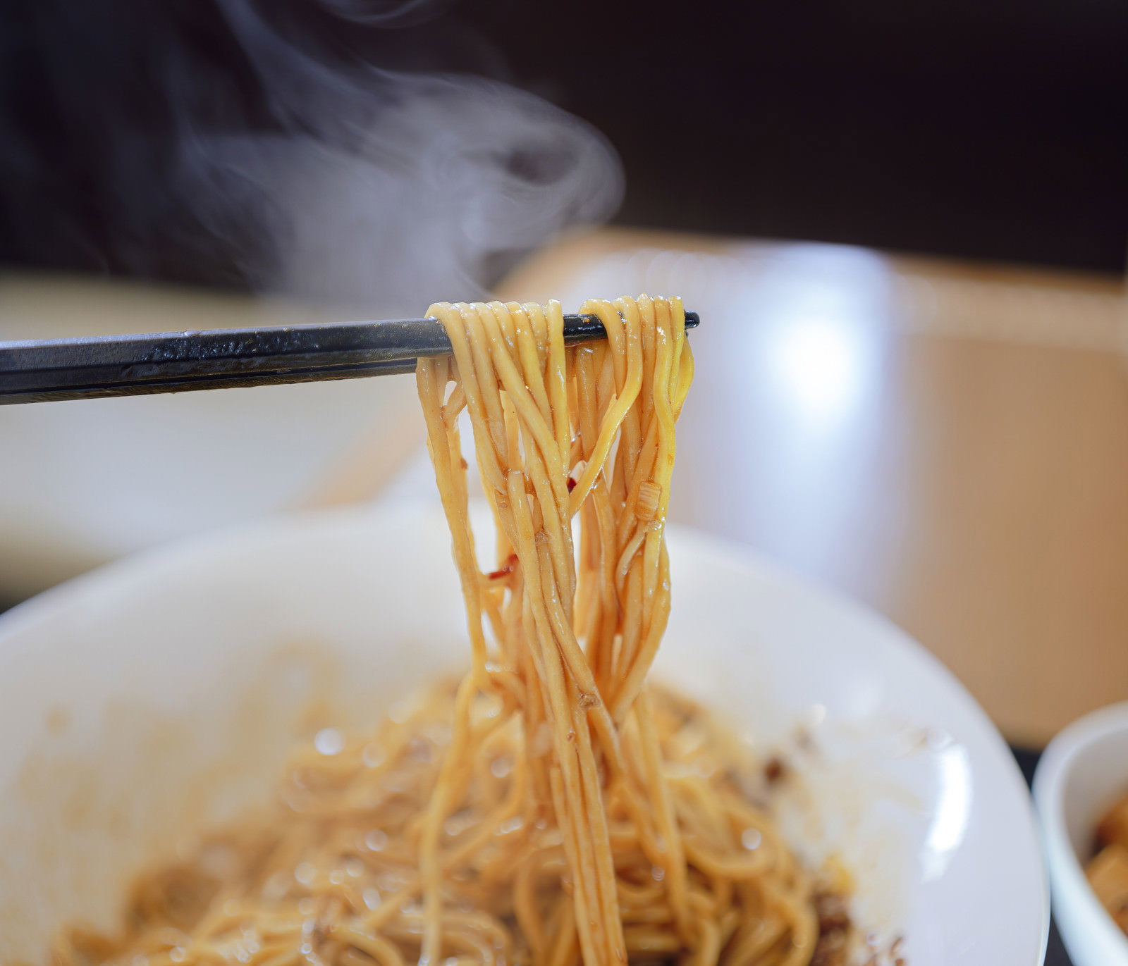 湯気が立ち上る汁なし担々麺を箸で持ち上げている様子