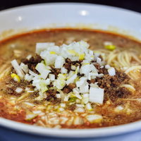 赤いスープが特徴の刻みネギが乗った担々麺の写真