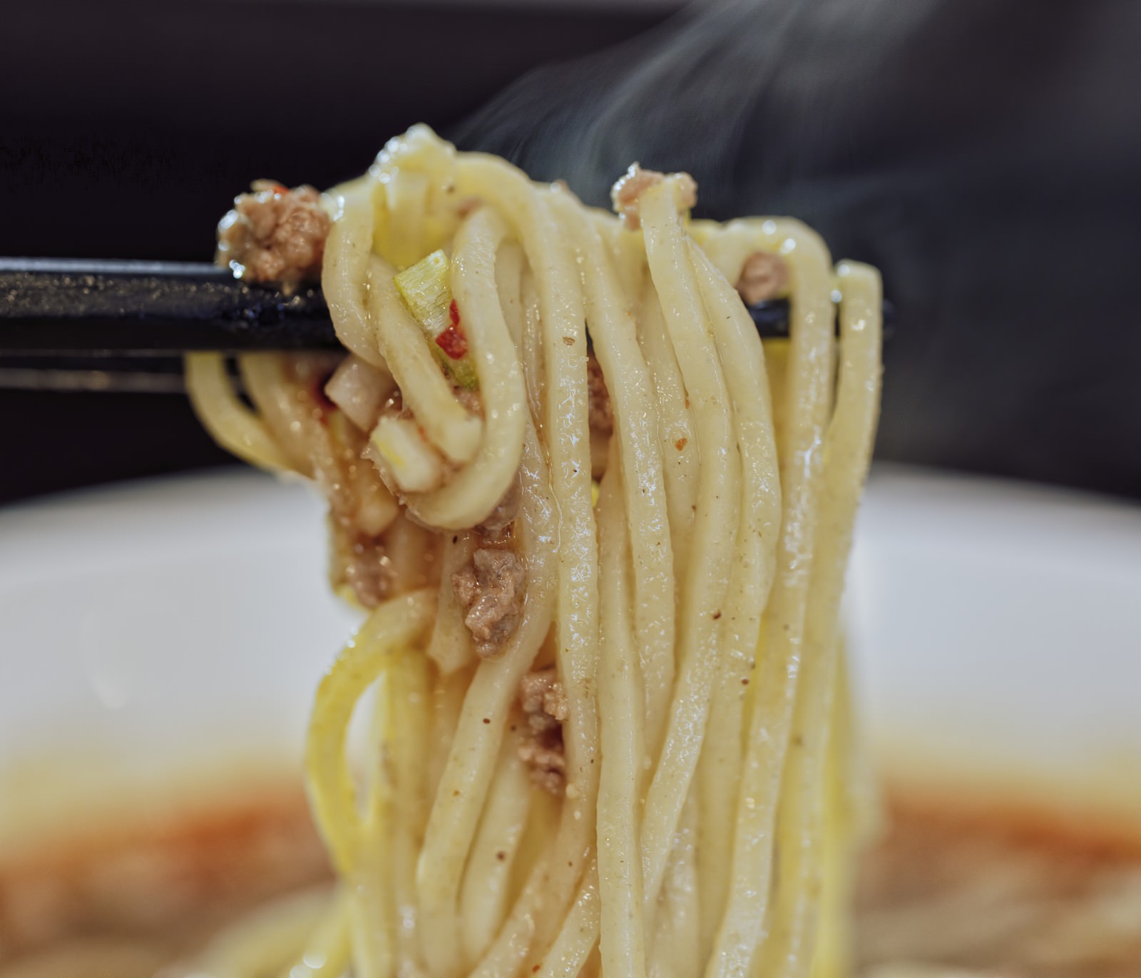 箸で持ち上げられた湯気の立つラーメンの麺