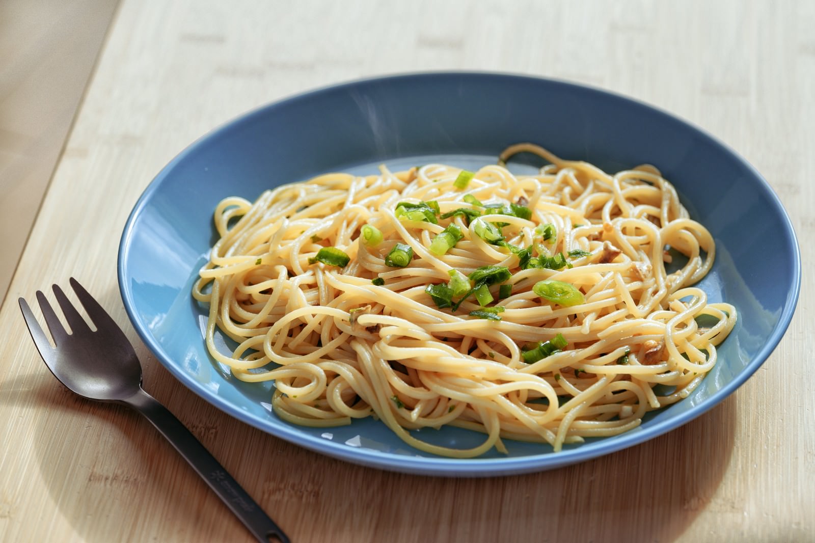 青い皿に盛られた和風スパゲティにネギが散らされている
