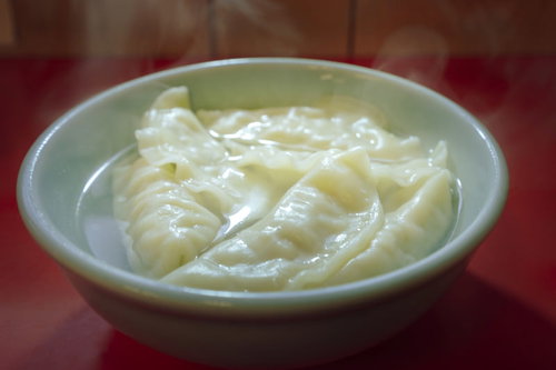 湯気が立つ水餃子を白い皿に盛った中華料理