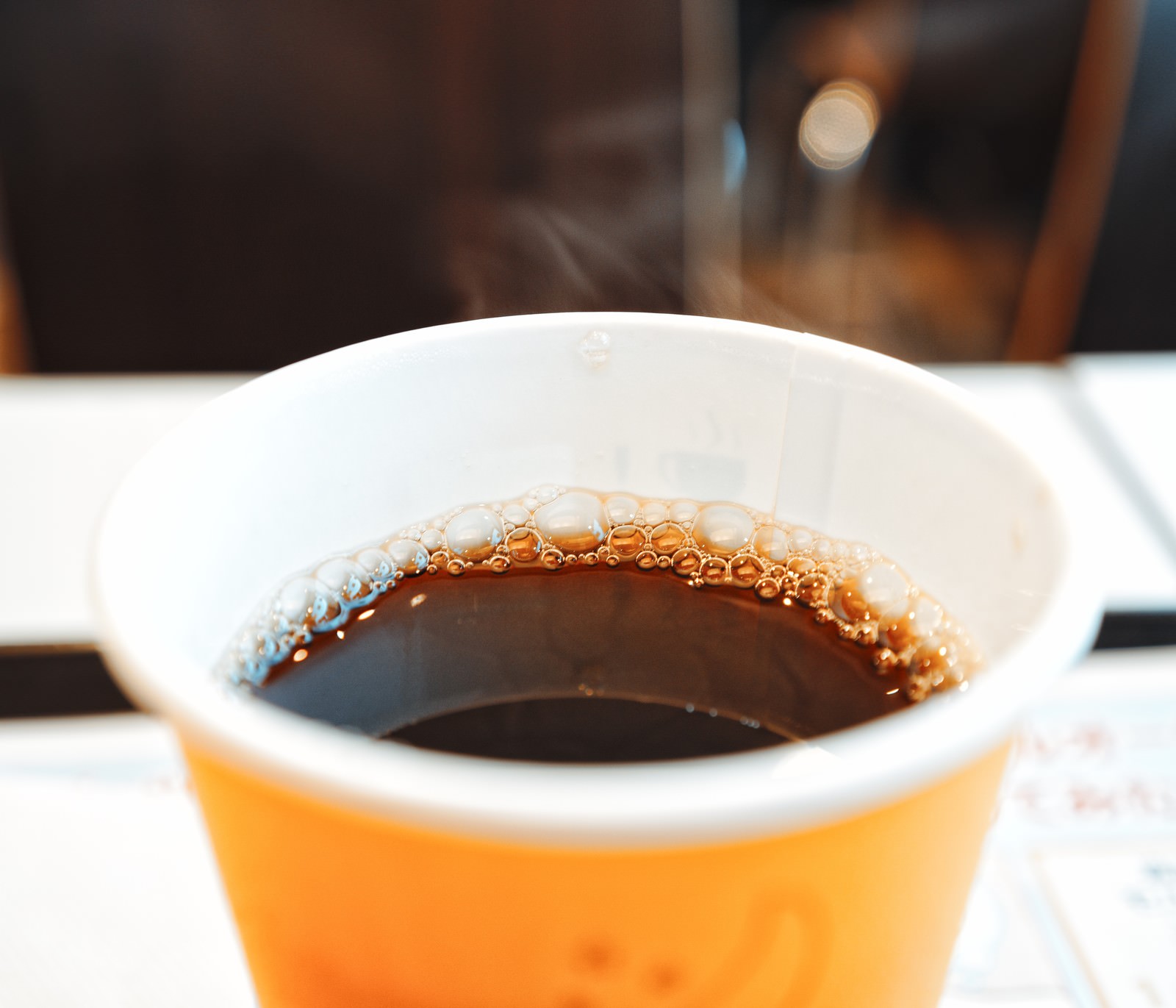 白いテーブルの上に置かれたオレンジ色の紙コップに入ったコーヒー