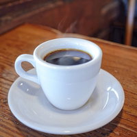 木製テーブルに置かれた淹れたてコーヒーとコーヒー豆の写真