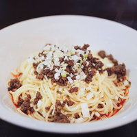 白い皿に盛った汁なし担々麺、ひき肉とねぎがトッピングされた中華料理の写真