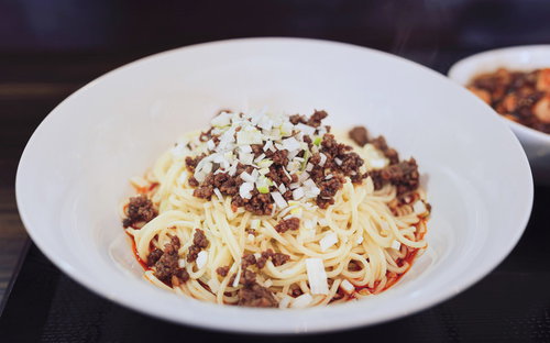 白い皿に盛った汁なし担々麺、ひき肉とねぎがトッピングされた中華料理