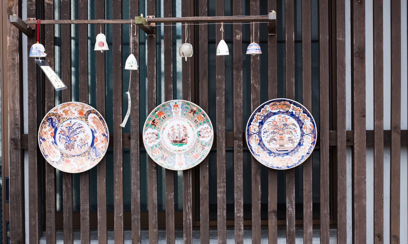 伊万里焼の皿と風鈴が木の格子壁に展示された光景