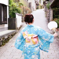 古い町並みを歩くうちわを持った浴衣女子の後ろ姿の写真