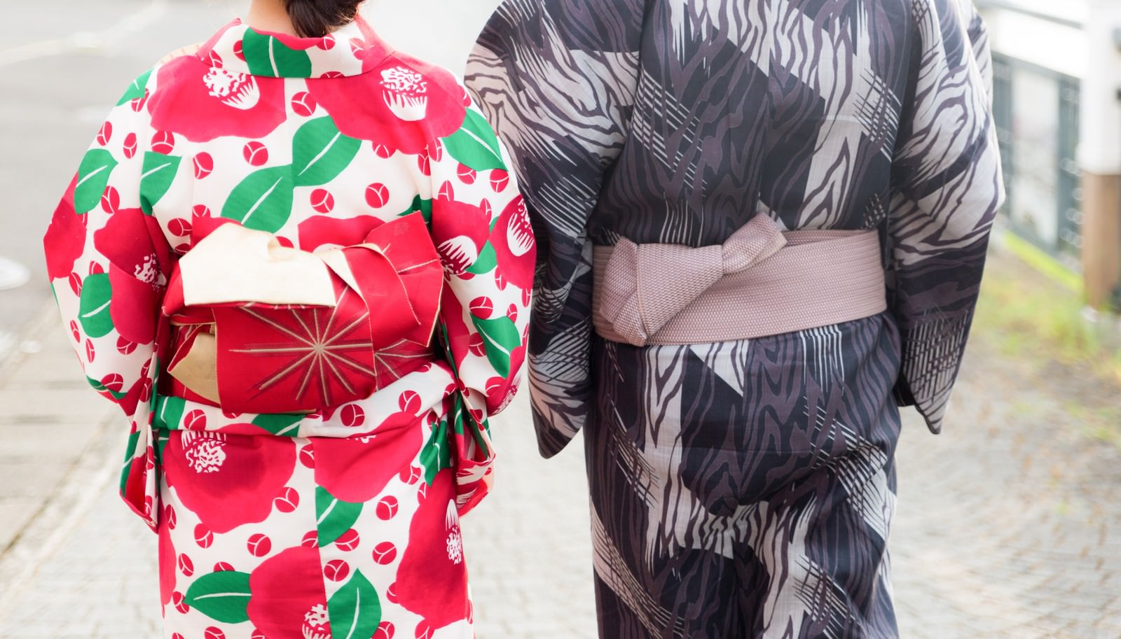 花柄と濃色の浴衣を着たカップルが石畳を歩く後ろ姿