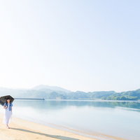 穏やかなイマリンビーチを日傘で歩く白い服の女性の写真