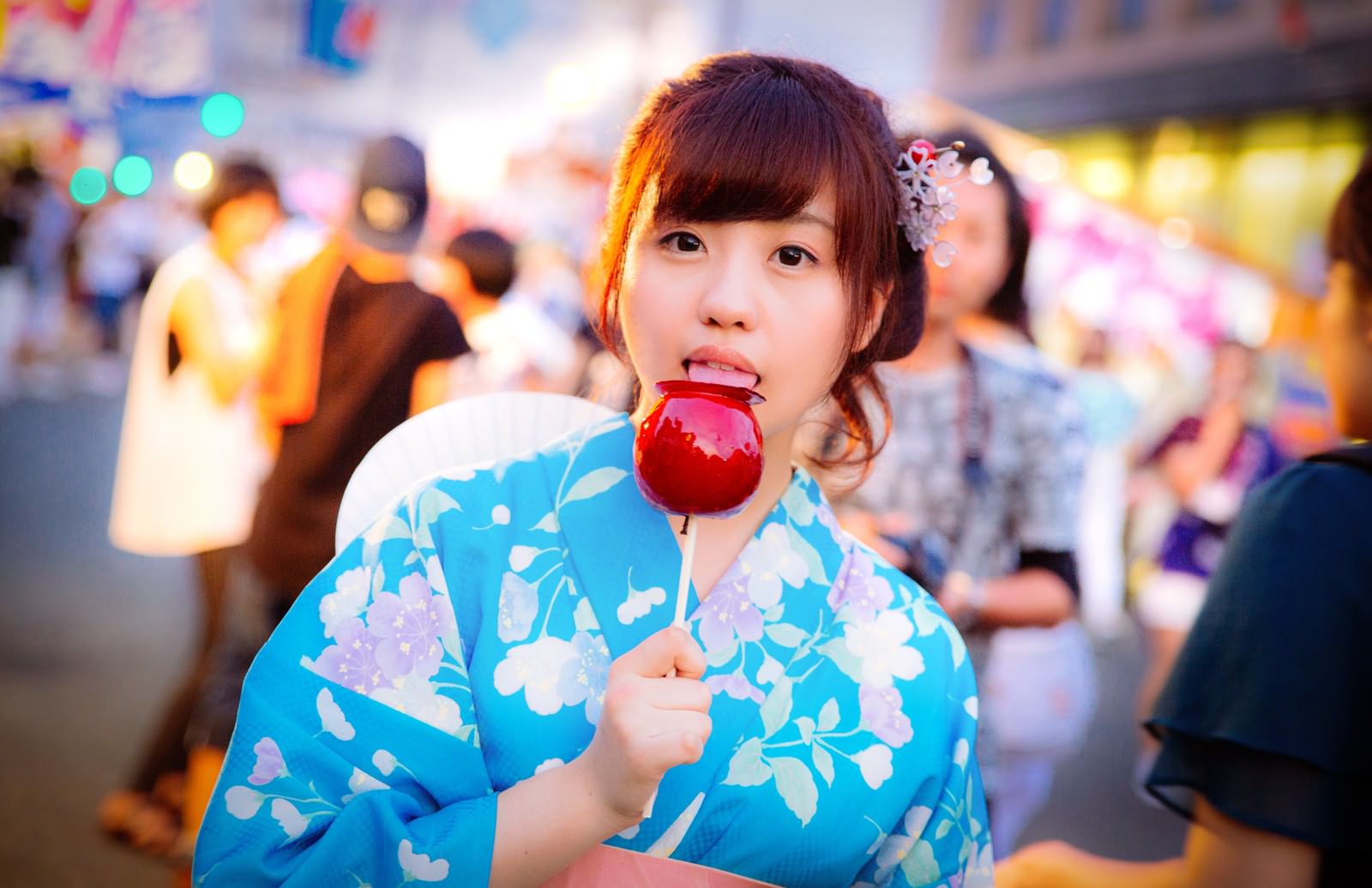 浴衣姿の女性がりんご飴を口元に近づける夜の縁日［モデル：河村友歌］