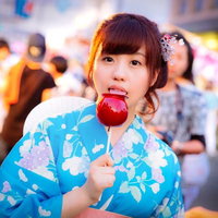 浴衣姿でりんご飴を食べる女性の夏祭り風景の写真