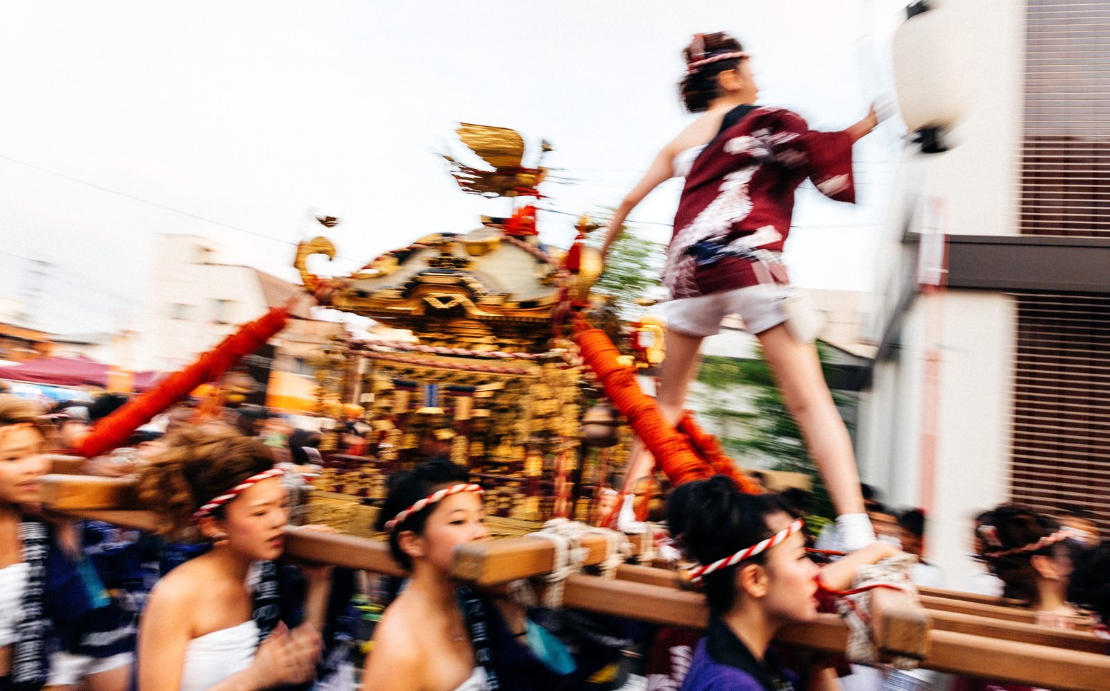 伊万里市のどっちゃん祭りで、赤と金色の帯を巻いた担ぎ手たちが豪華に装飾された女神輿を力強く掲げている