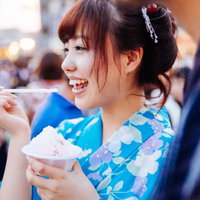 祭りの屋台でかき氷を食べて喜ぶ浴衣姿の女性の写真