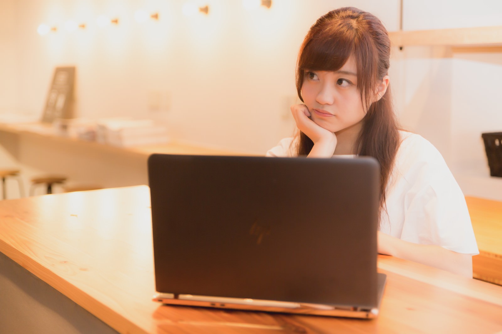 ノートパソコンの前で頬杖をついて悩む女性［モデル：河村友歌］