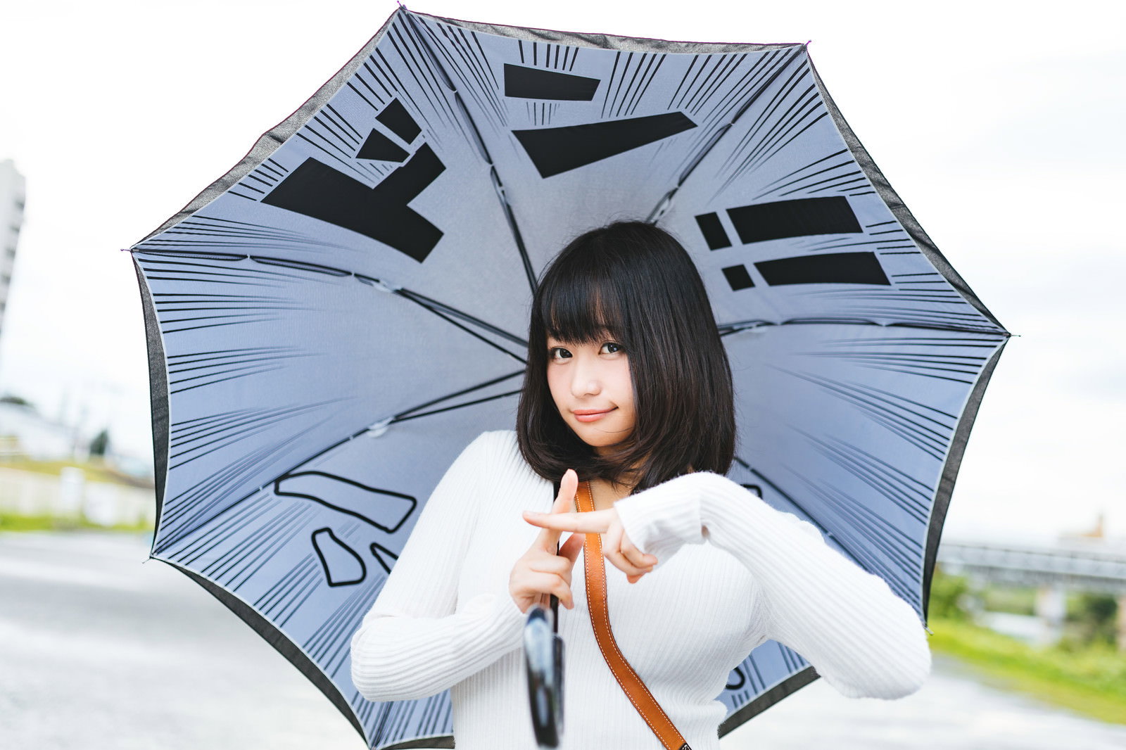 青い傘を持ちながら両手で印を結ぶポーズをとる白いニット姿の女性［モデル：茜さや］