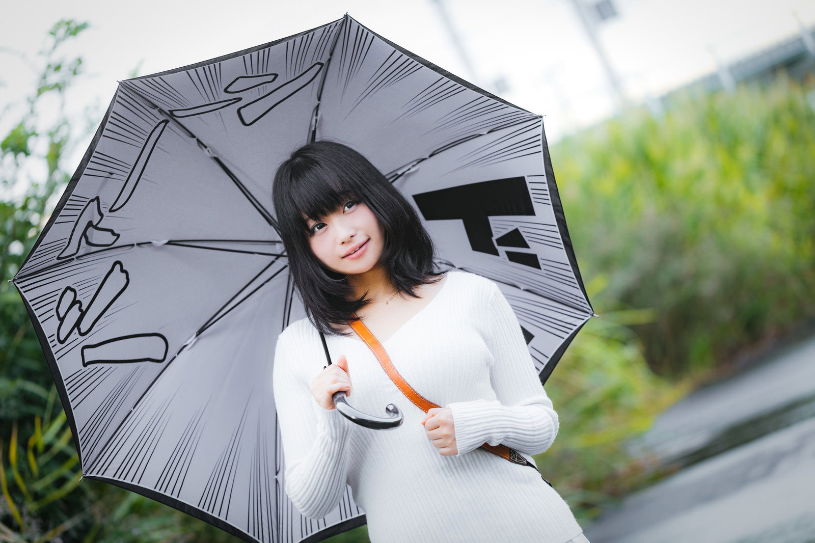 白い服を着て灰色の傘を差した女性が微笑んでいる様子［モデル：茜さや］