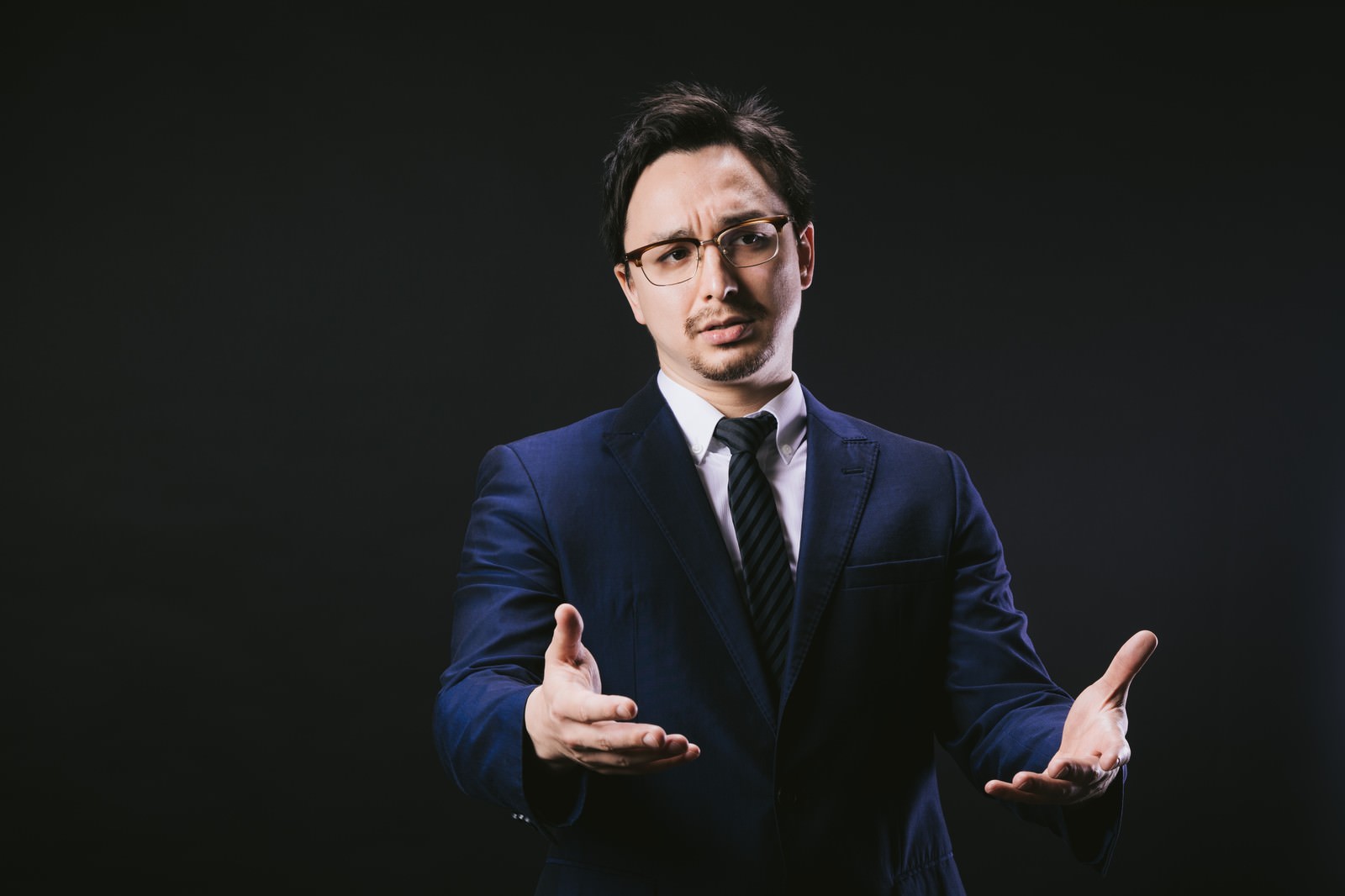 スーツを着た男性が両手を広げて困惑の表情を見せている［モデル：Max_Ezaki］