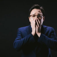 口を抑えて絶望するドイツ人ハーフの男性、年収低下による失敗と困窮の表情の写真