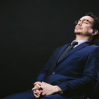 リクライニングチェアで寝落ちする紺色スーツの会社員の写真