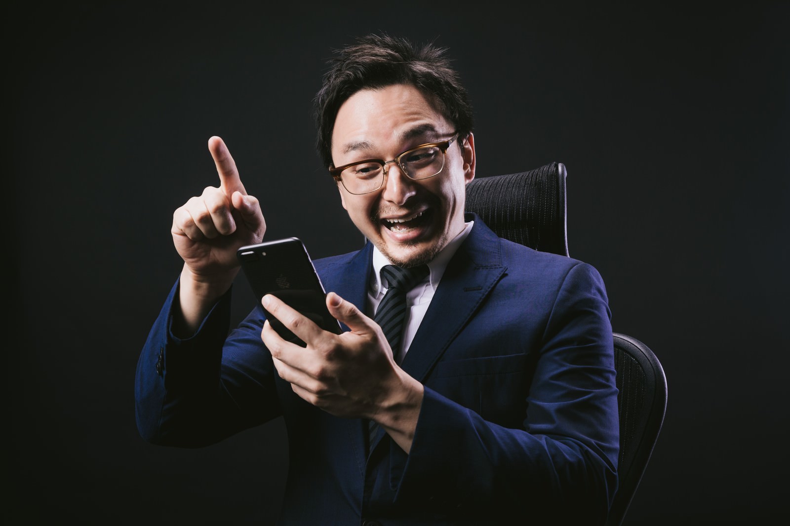 スーツを着た眼鏡の男性がスマートフォンを操作している様子［モデル：Max_Ezaki］