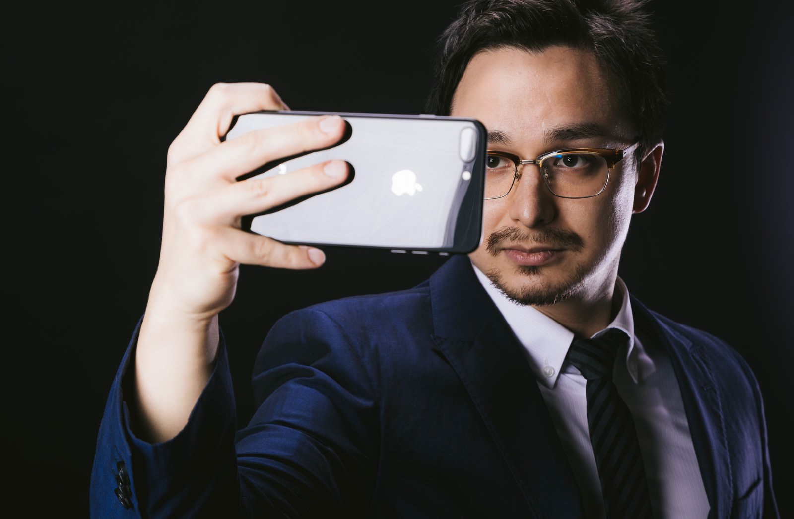 スマートフォンで自撮りをする眼鏡をかけたスーツ姿の男性［モデル：Max_Ezaki］