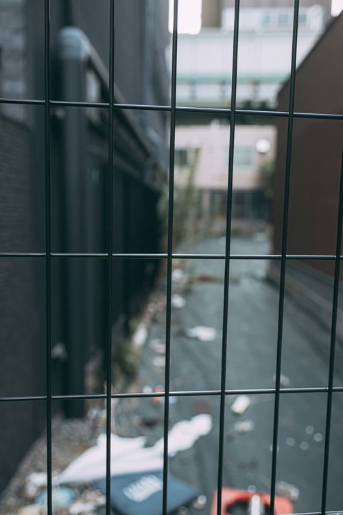 ゴミが散らかる路地裏のワイヤーフェンス越しの風景