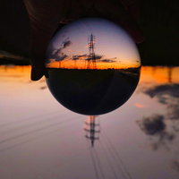 水晶玉に映る夕焼けと鉄塔のシルエット、送電線のある風景の写真