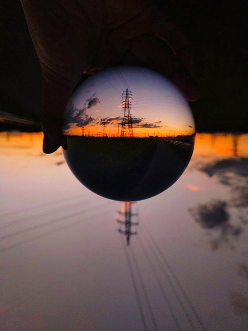 水晶玉に映る夕焼けと鉄塔のシルエット、送電線のある風景