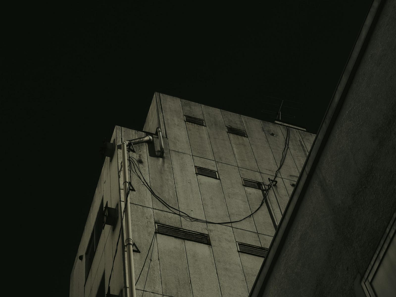 コンクリートの外壁に配管が這うビルを下から見上げた構図