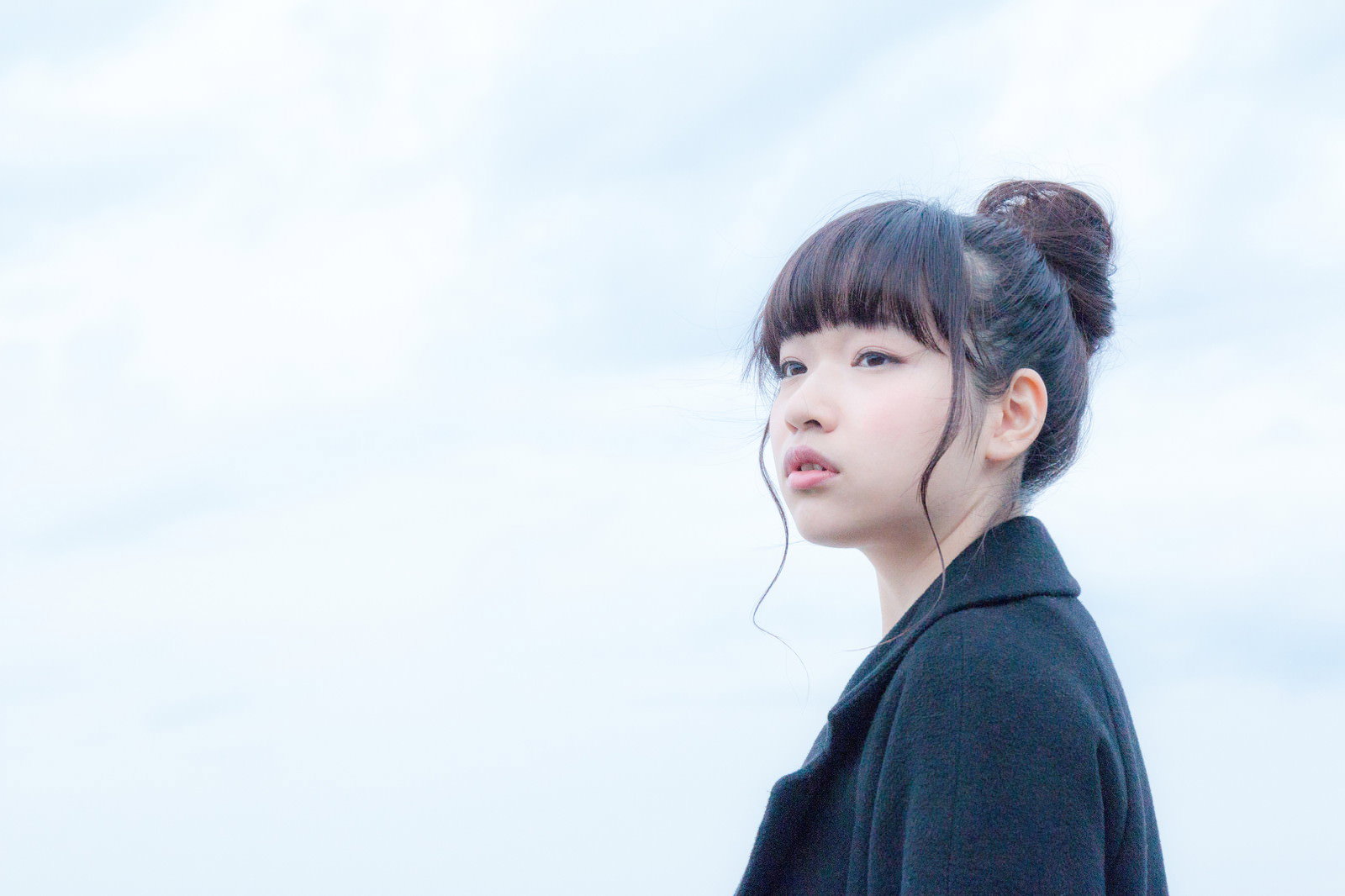 黒いコートで冬空を見上げる女性の横顔［モデル：渡辺友美子］
