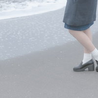 波打ち際でたたずむ女性の足元、白いソックスと厚底シューズの写真