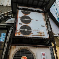 老朽化したビルの壁に設置された複数の業務用エアコン室外機の写真