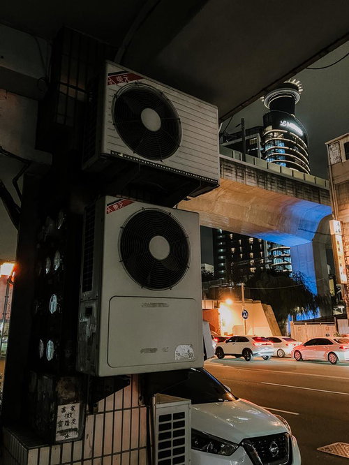 古びたエアコン室外機が並ぶ雑然とした夜間のビル裏路地