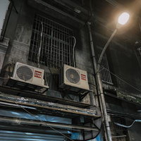 夜の路地裏に佇むエアコン室外機と街灯の灯りの写真