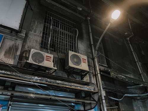 夜の路地裏に佇むエアコン室外機と街灯の灯り