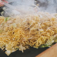 屋台で提供される焼きそば、ねぎやもやしをトングで炒める調理風景の写真