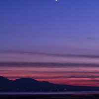 夕暮れの空に浮かぶ三日月と海岸のシルエットの写真
