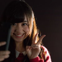 暗い場所で自撮りピースサインをする笑顔の女性の写真