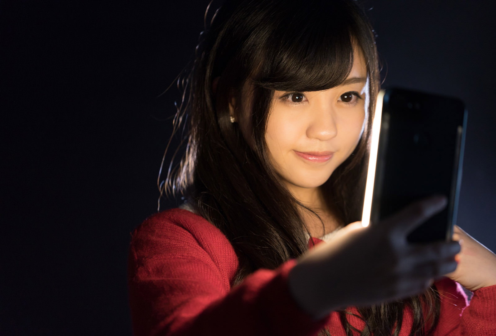 自撮りライトを使ってスマートフォンで撮影する笑顔の女性［モデル：河村友歌］