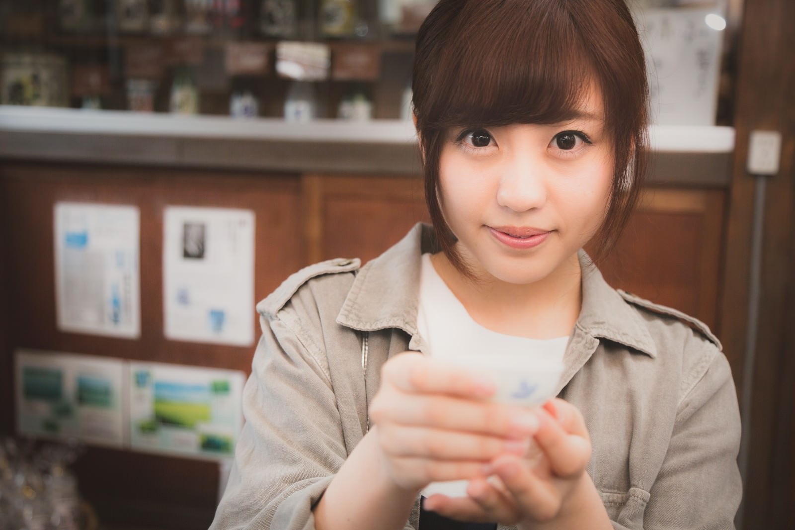 おちょこを手に日本酒の試飲を勧める笑顔の女性［モデル：河村友歌］
