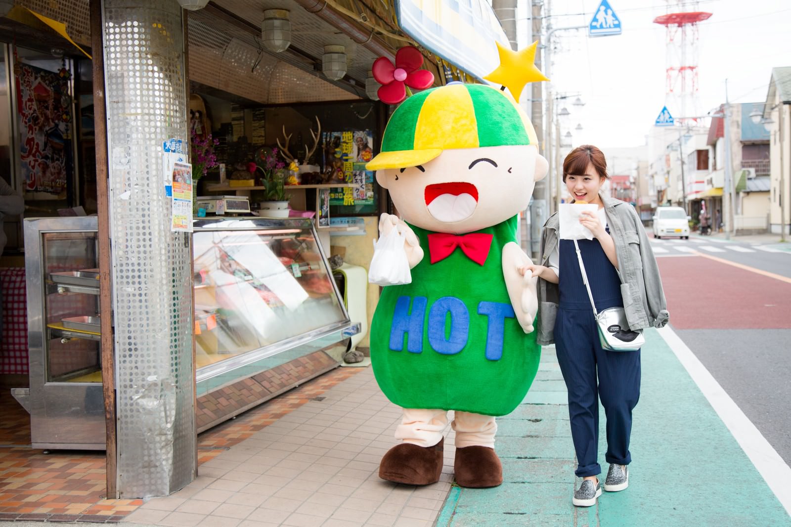 商店街を歩くゆるキャラと女性［モデル：ホットくん 河村友歌］