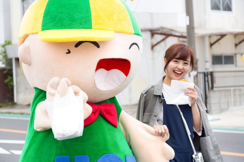 大原中央商店街のゆるキャラと笑顔でコロッケをほおばる女性