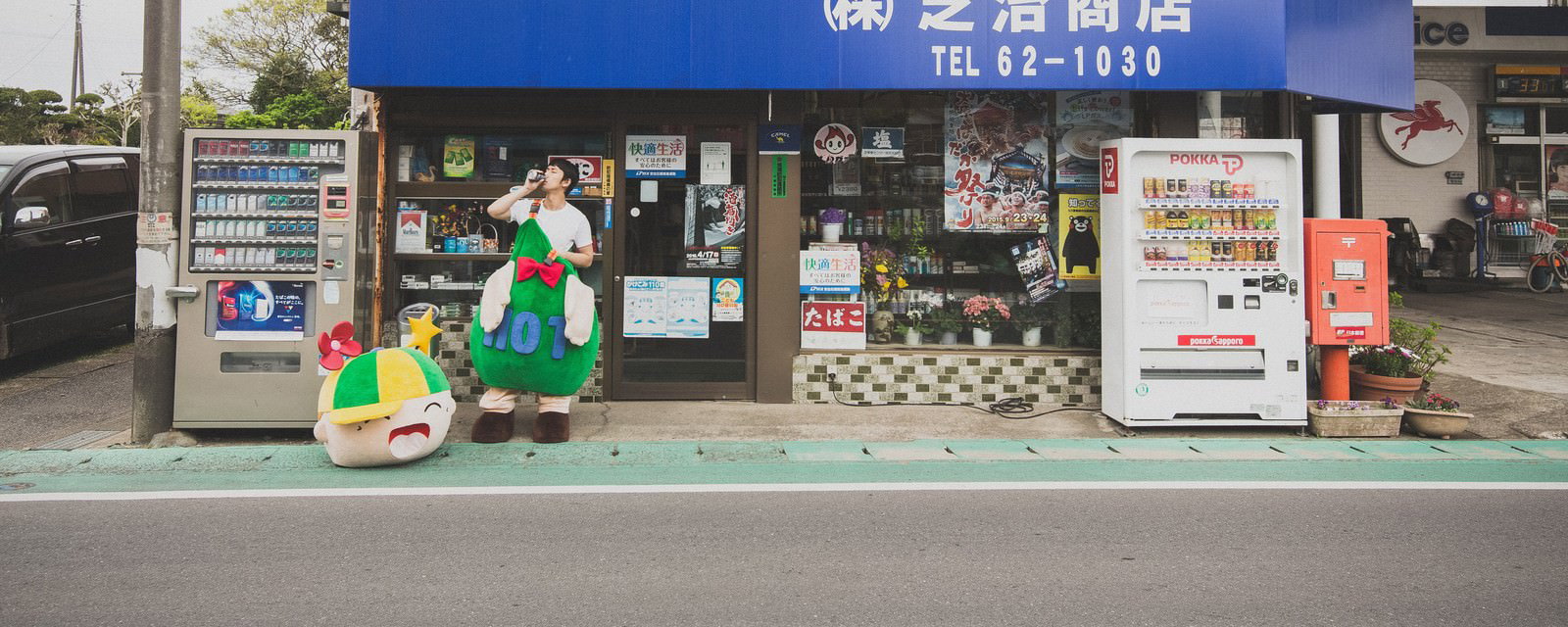 大原中央商店街の商店前でコーヒーを飲むゆるキャラと男性［モデル：大川竜弥 ホットくん］