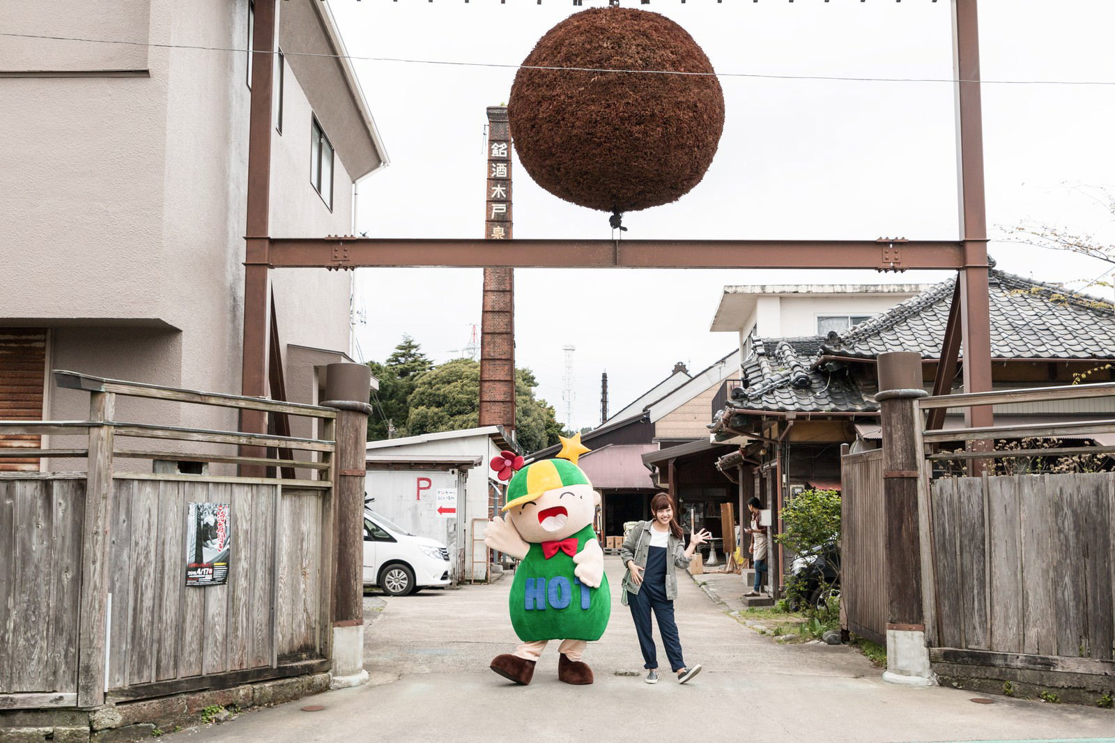 大原中央商店街の蔵元前に立つゆるキャラと女性［モデル：ホットくん 河村友歌］