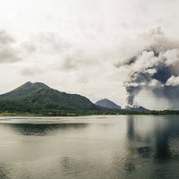 高台から見下ろす噴煙を上げる火山島と青い海の写真