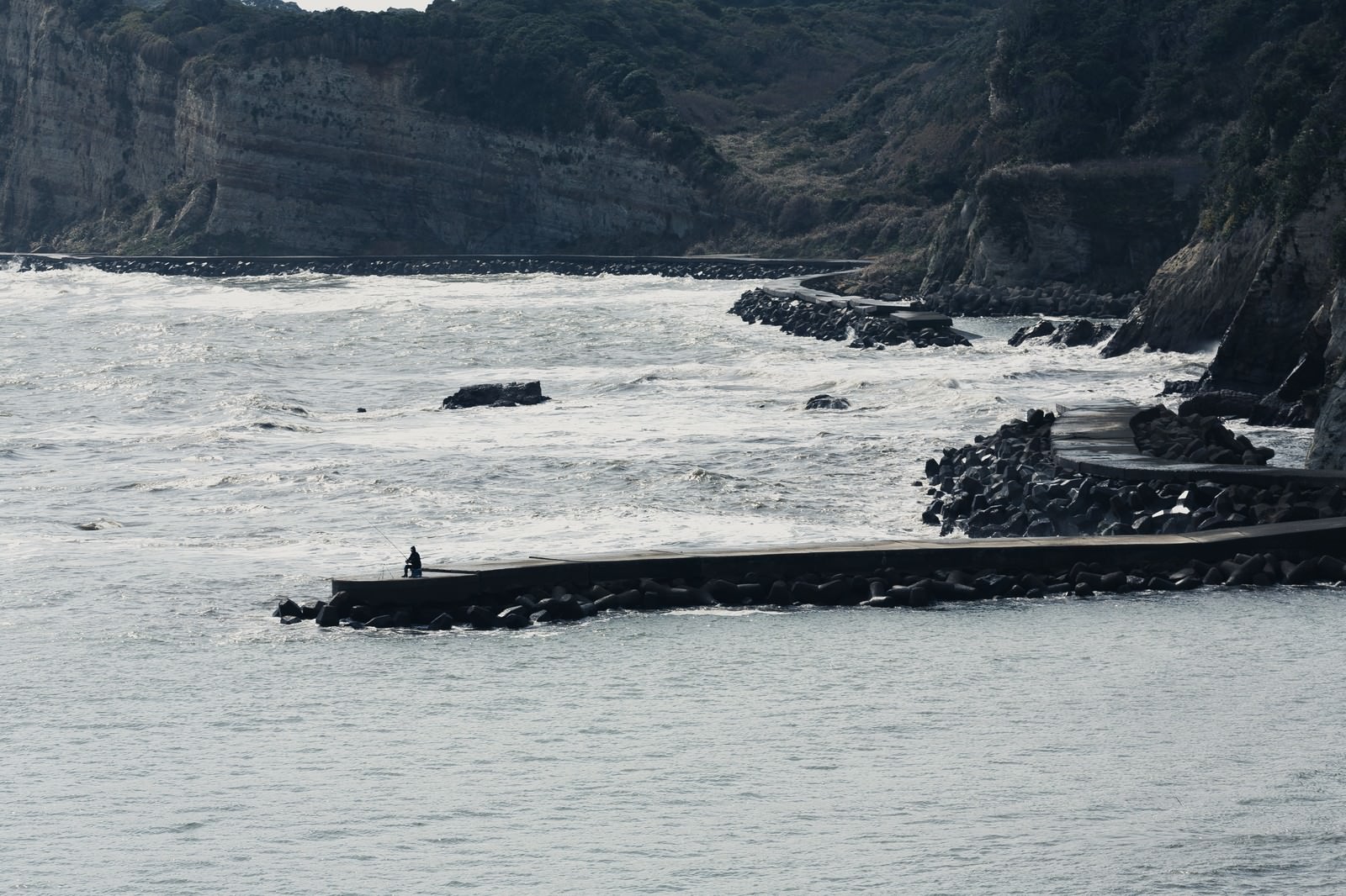 千葉県いすみ市の崖に囲まれた海岸で防波堤から釣りをする人