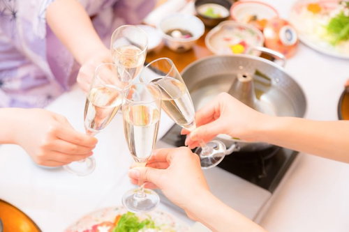 食事のテーブルで4人の手がグラスを中央で合わせる乾杯の瞬間