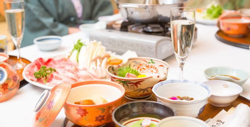 窓から自然光が差す室内テーブルに肉や野菜と鍋料理が並ぶしゃぶしゃぶ